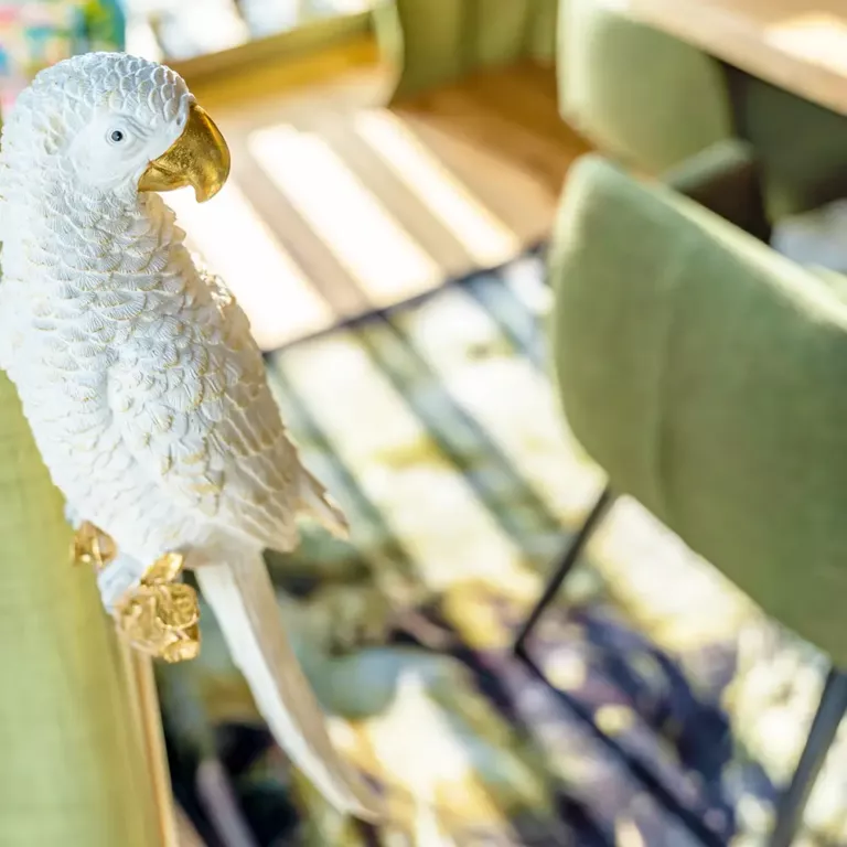 Close-up of a white parrot sculpture with gold accents in a stylish, sunlit interior.