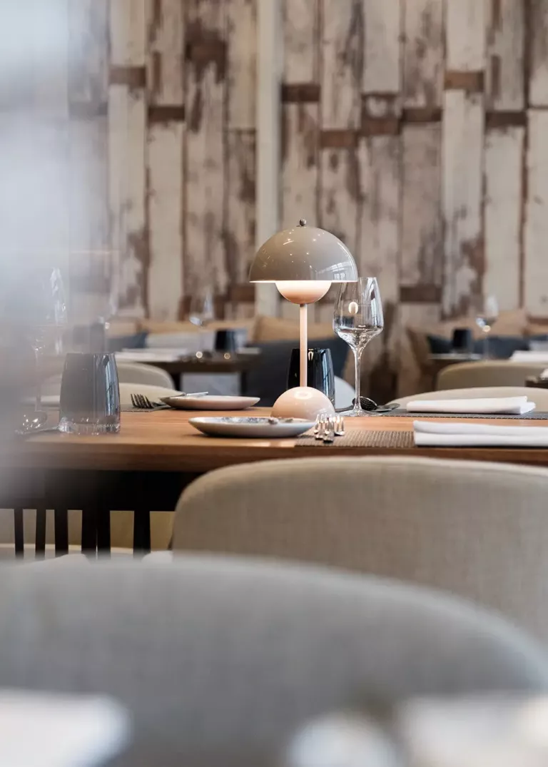 Stylishly set table in a modern restaurant with a designer table lamp, wine glass, and rustic wooden wall in the background.