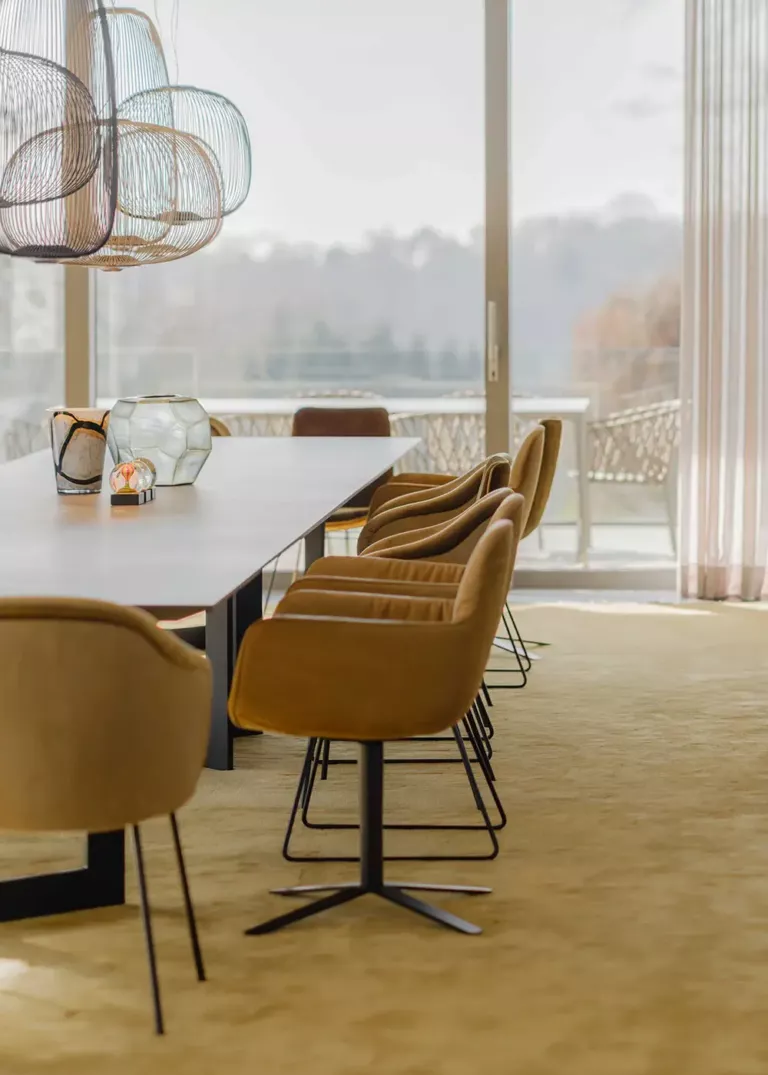 Modern conference room with large windows, elegant cognac-colored chairs, and a stylish wire pendant light.