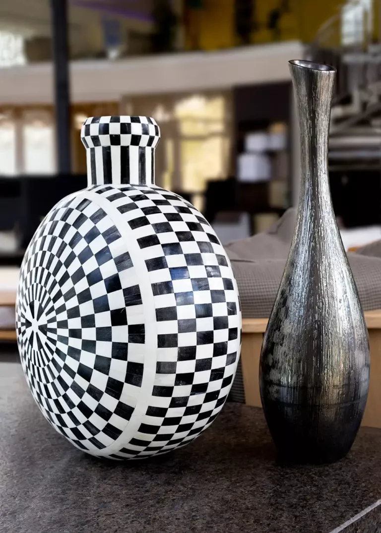 Two decorative vases on a dark surface, one with a black and white checkerboard pattern and a tall, slender vase with a metallic finish.