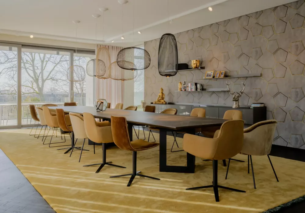 Modern dining room with a large wooden table, mustard-colored chairs, and geometric wall paneling. Pendant lights and floor-to-ceiling windows overlooking the terrace create a bright ambiance.
