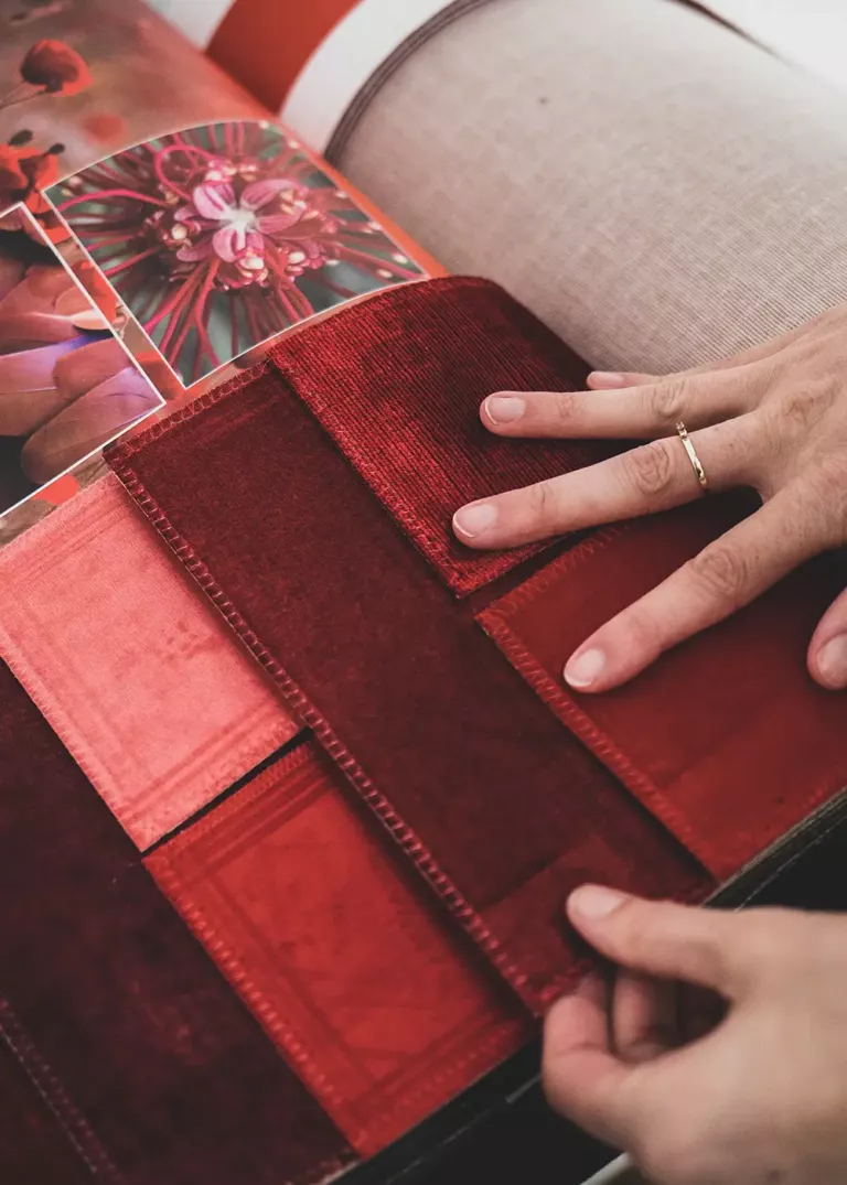 Hand examining a selection of red fabric samples in a design book, inspired by floral motifs.