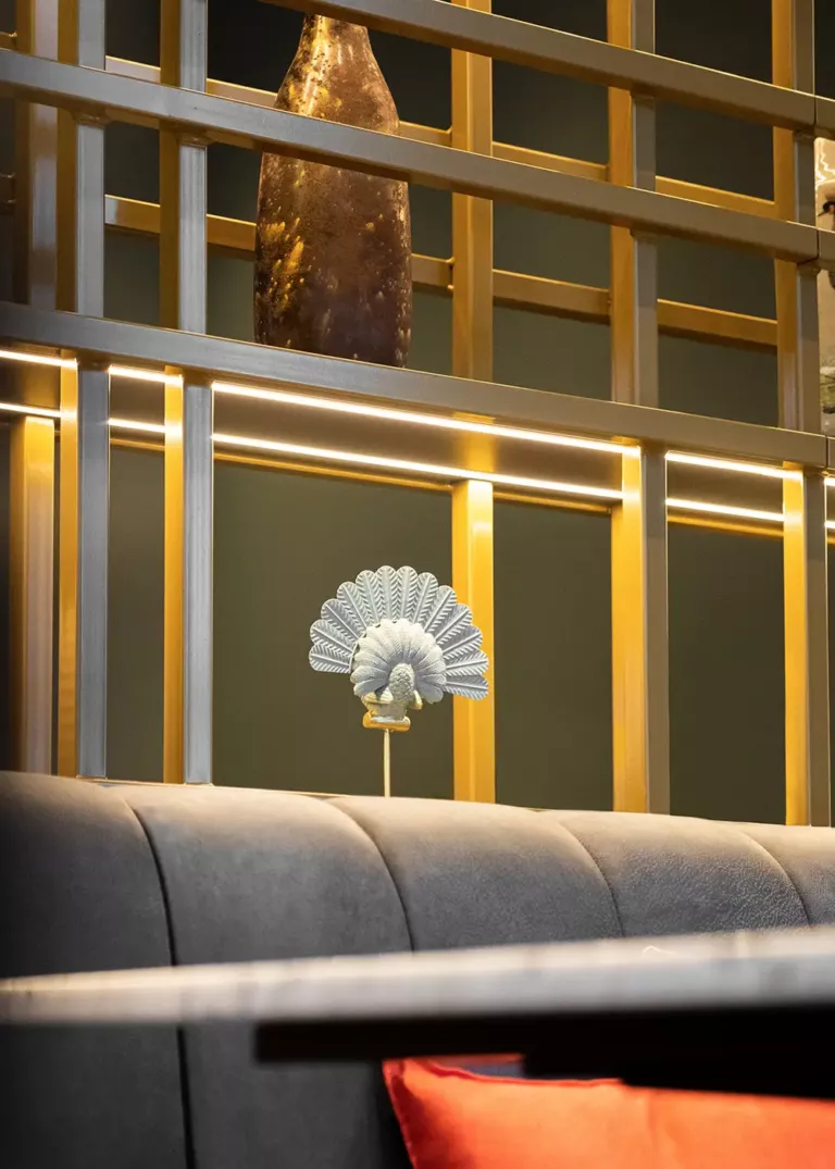 Close-up view of a modern shelving unit with gold metal bars and integrated lighting. Decorative elements such as a bronze-colored vase and a delicate peacock figurine enhance the design.