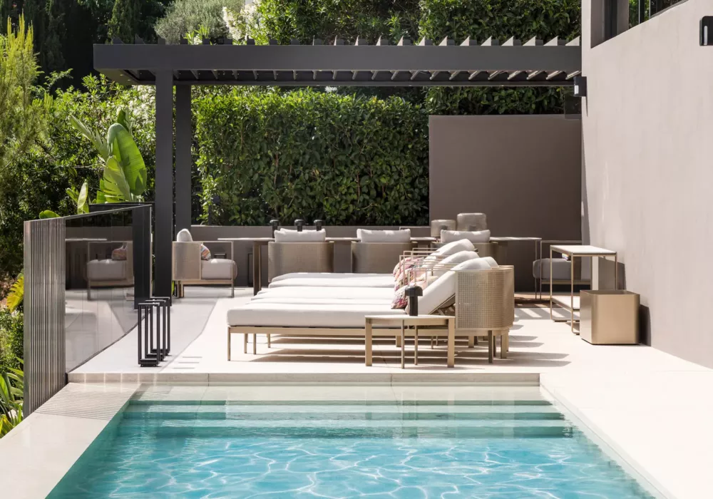 Luxurious pool terrace with modern sun loungers, comfortable seating, and a stylish pergola. Surrounded by lush greenery for a relaxing ambiance.