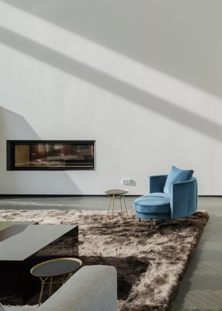 Minimalist living room with a blue velvet armchair, plush rug, modern fireplace, and elegant side tables.