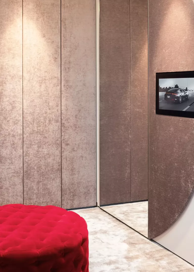 Elegant room with textile wall panels, mirrors, integrated screen, and a red tufted ottoman as an accent piece.