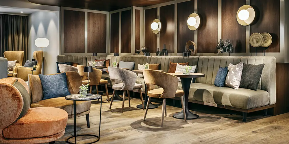 Elegant lounge area with upholstered benches, cozy armchairs, stylish wood-paneled walls, and ambient lighting.