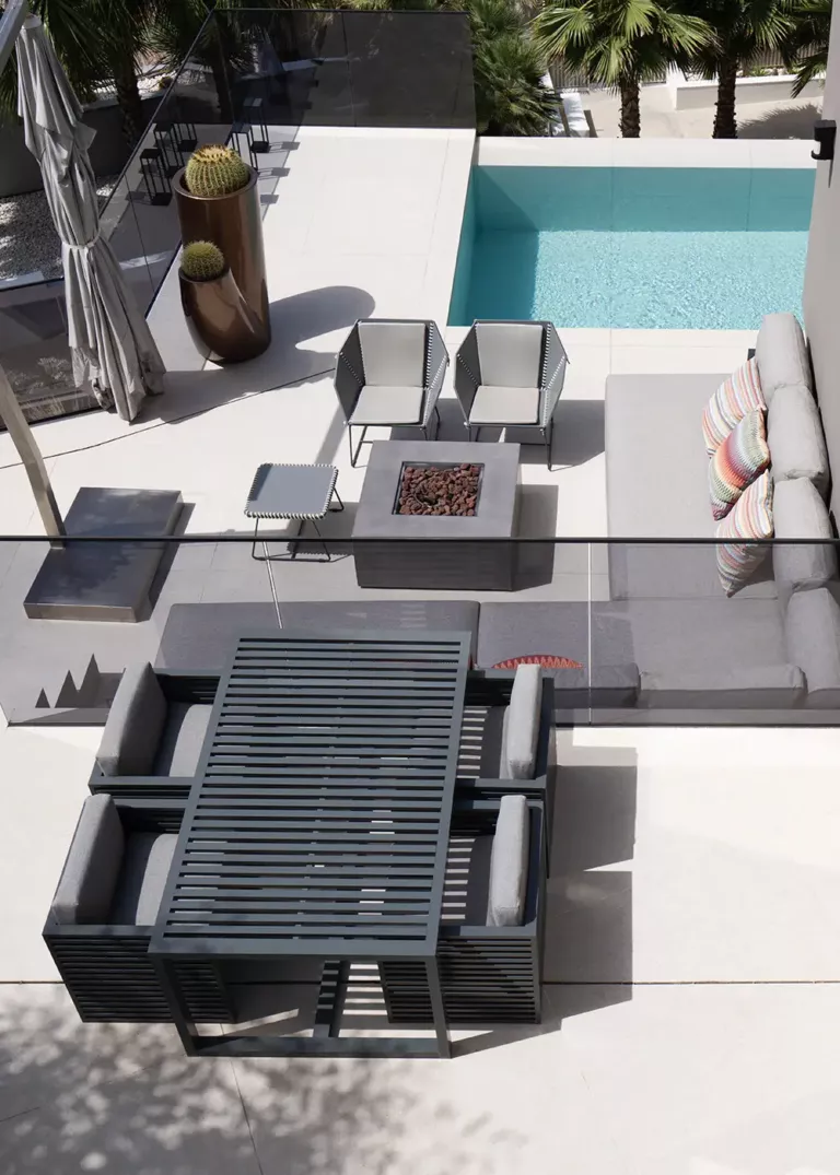 Modern pool terrace with stylish outdoor furniture, a fire pit, and a dining table. Subtle gray tones and decorative accents create an elegant ambiance.