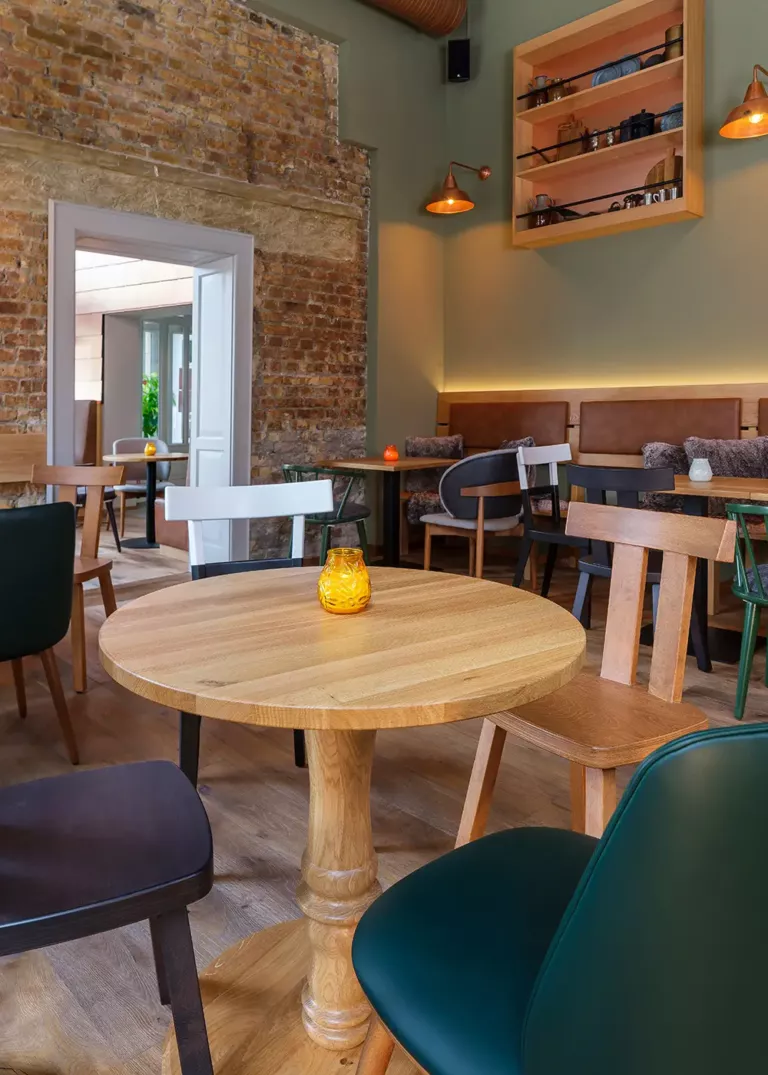 Cozy restaurant with a rustic brick wall, wooden tables, mixed chairs, and candle lighting.