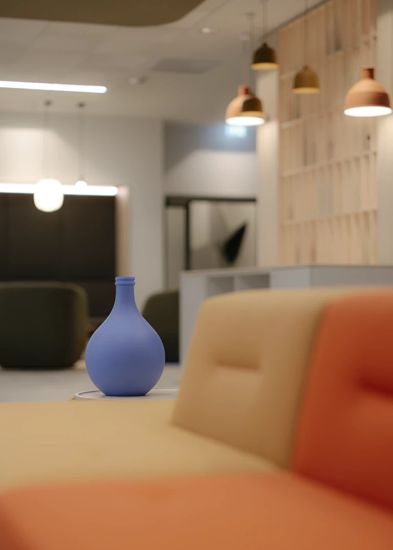 Modern interior design featuring a matte blue vase on a side table in the foreground. In the background, upholstered seating in warm tones, hanging pendant lights in earthy shades, and a shelving unit with decorative elements complete the space.
