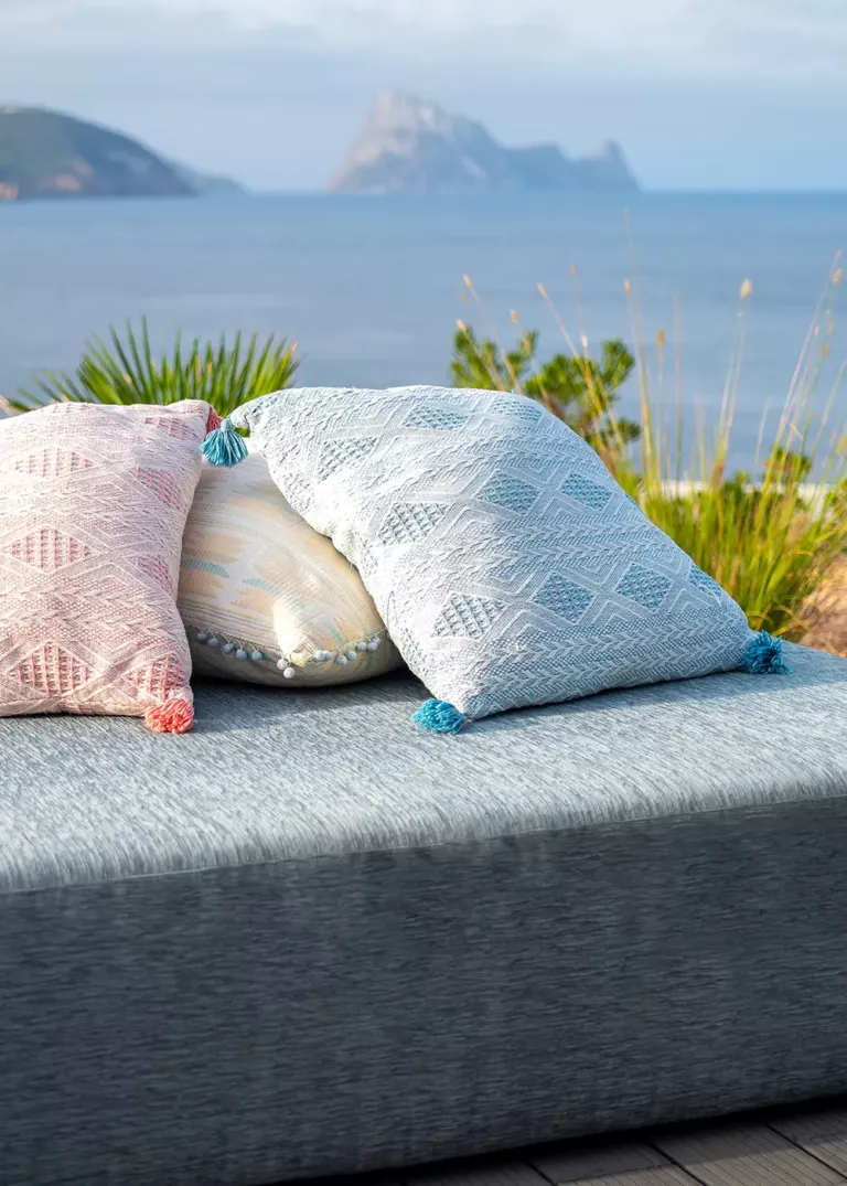 Relaxing outdoor lounge at 7Pines Resort Ibiza with decorative pillows and a view of the sea and the rocky island of Es Vedrà