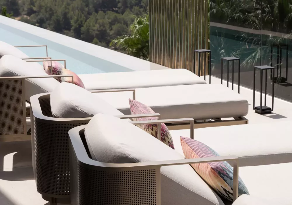 Luxurious pool terrace with beige sun loungers and stylish lounge chairs, decorated with patterned cushions. Elegant design featuring a modern railing and ambient lighting.