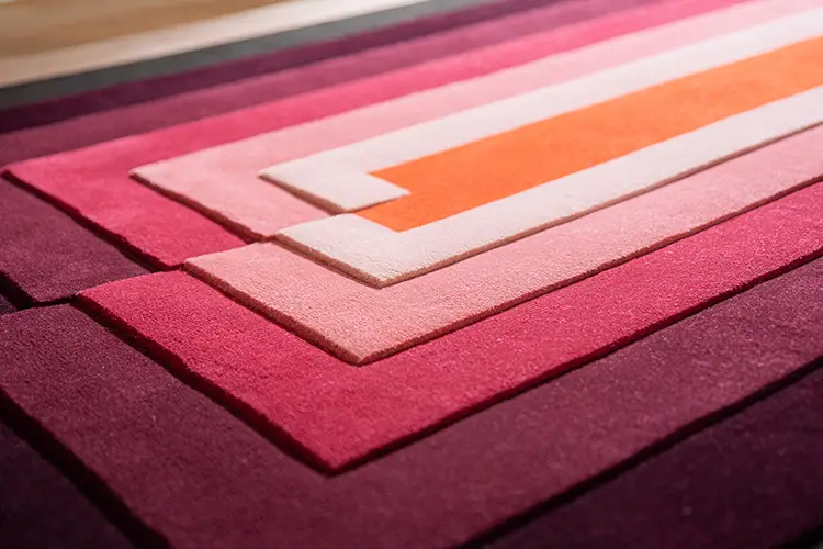 Close-up of a geometric design rug with layered shades of red and a vibrant orange accent line.